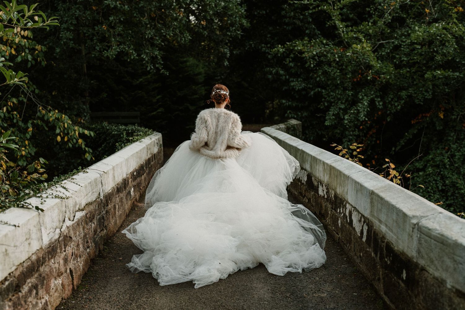 A flowing white wedding dress cascades over stone steps in a garden setting.