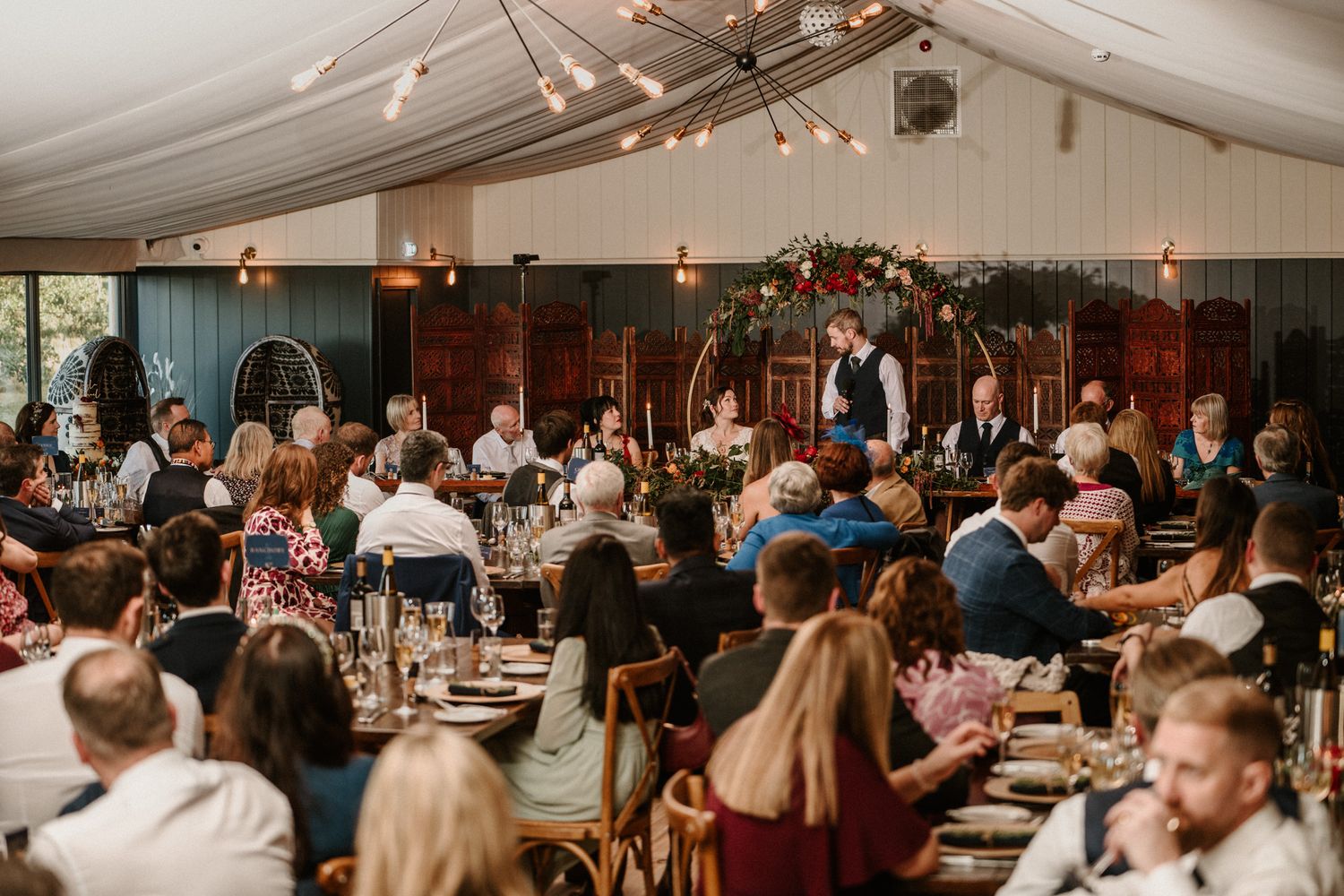 Wedding reception guests dancing and celebrating under string lights in an indoor venue.