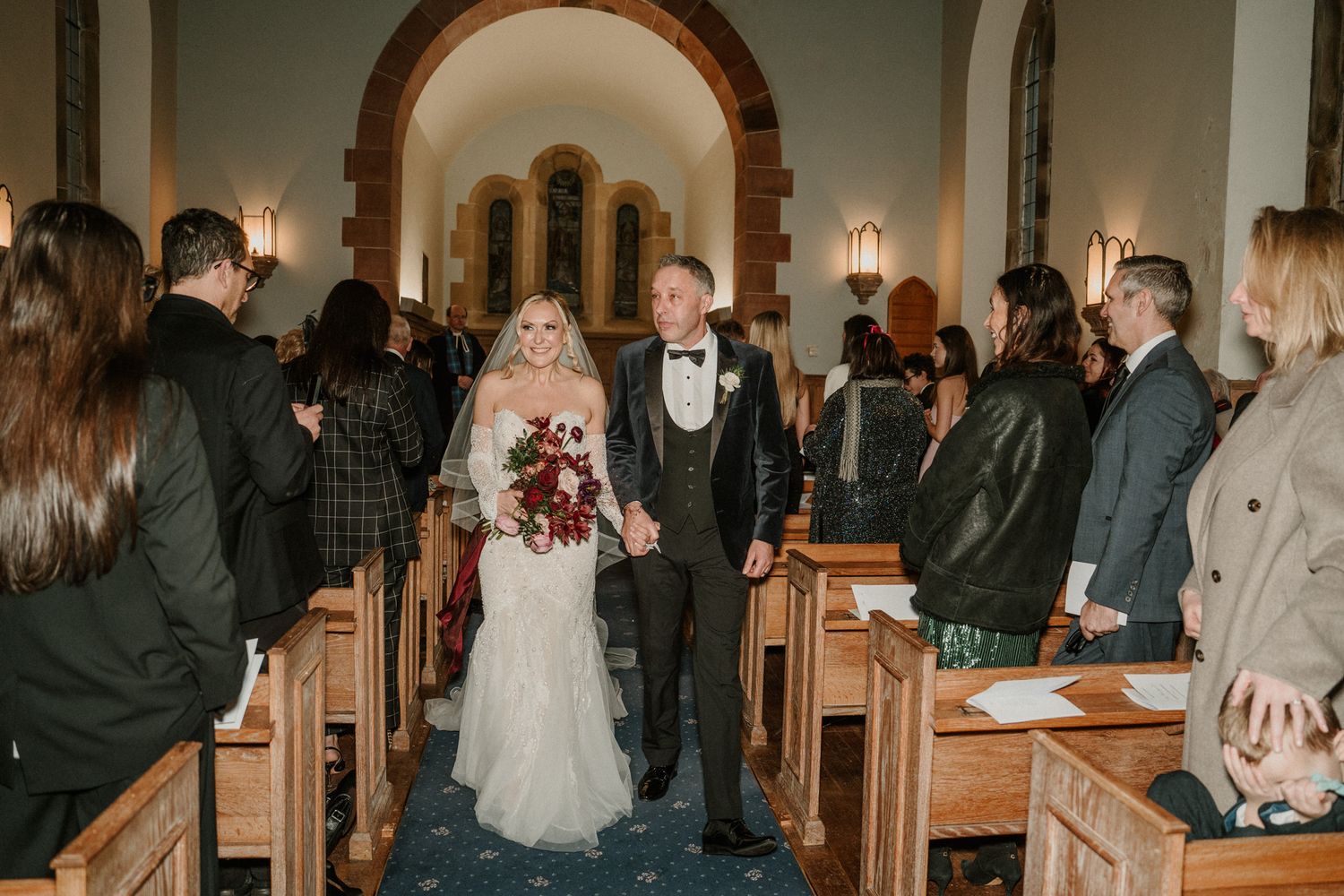 Wedding guests seated in wooden pews during indoor church ceremony.