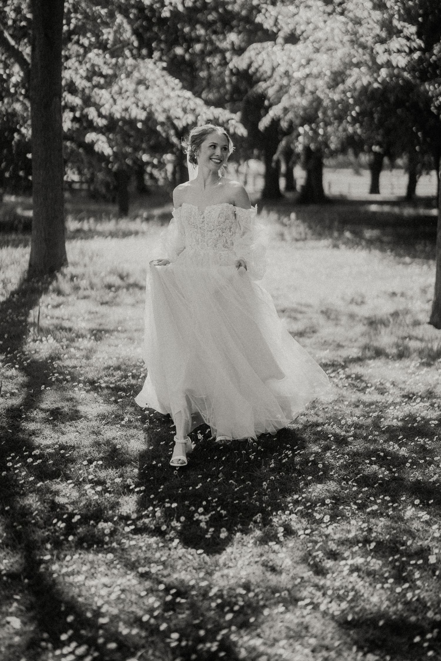 Black and white photo of bride twirling in flowing dress among scattered petals.