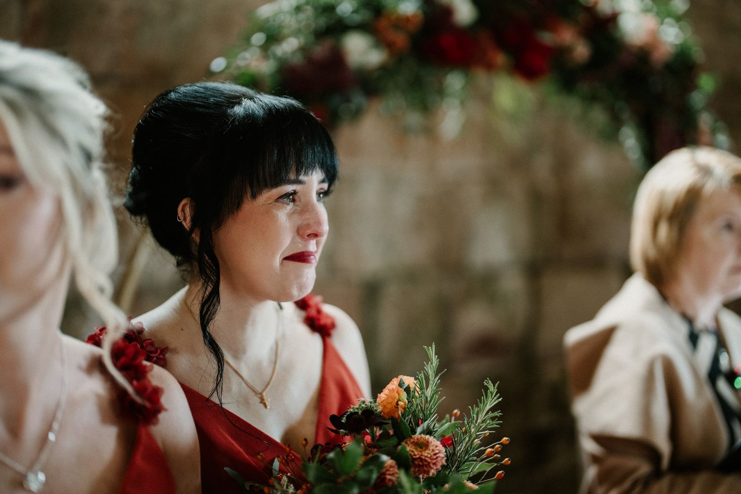 Elegant floral arrangements with red and orange blooms decorate stone church interior.