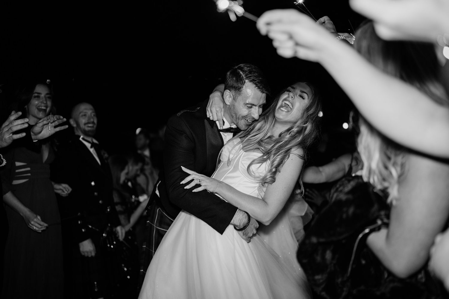 Wedding reception guests dancing and celebrating on a dark dance floor with dramatic lighting.