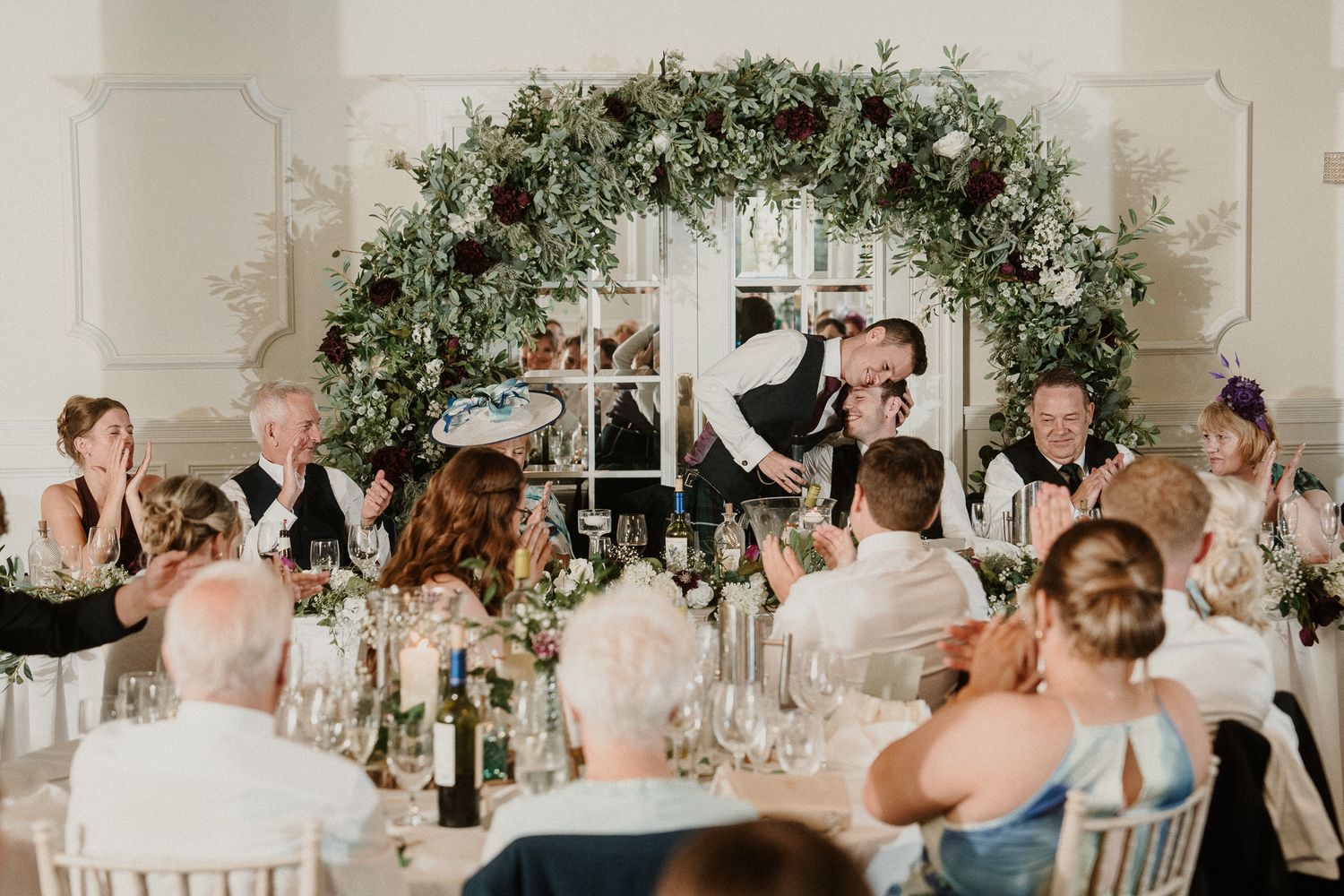 Wedding reception tables adorned with lush greenery and floral arrangements in an elegant white room.