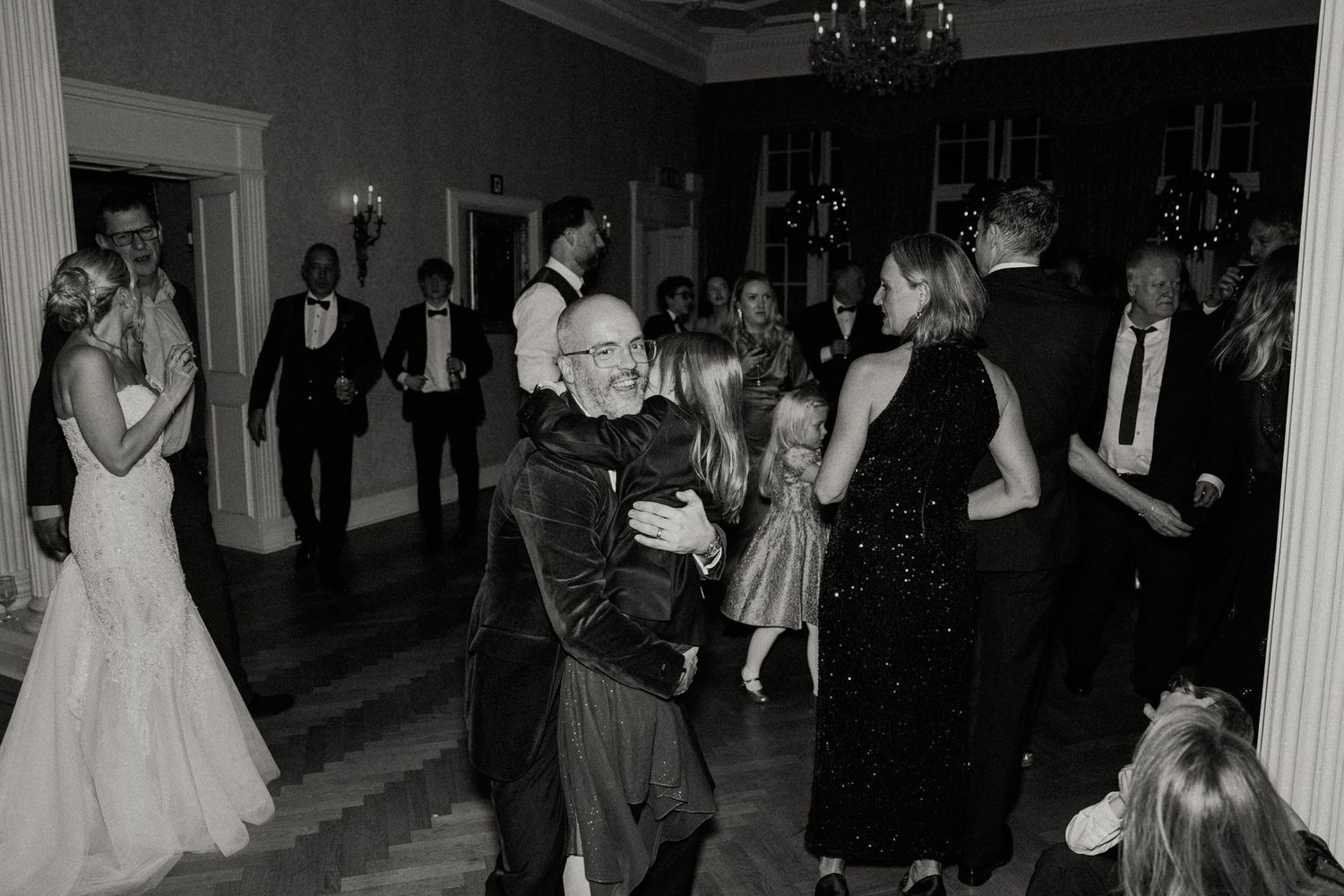 Wedding celebration in a grand ballroom with guests dancing under crystal chandeliers.