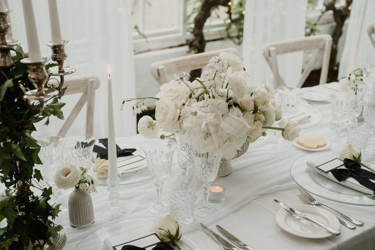 Elegant white wedding table setting with floral centerpiece and crystal glassware.