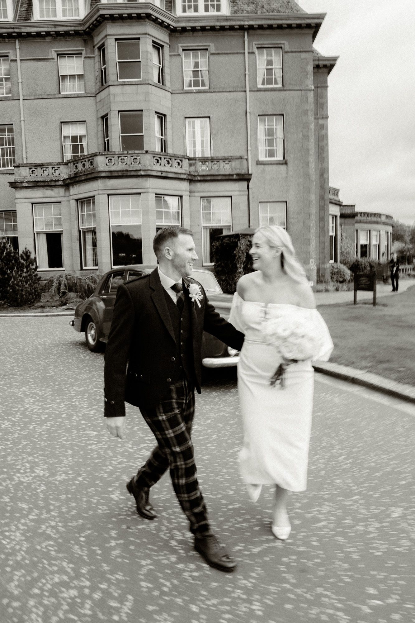 Black and white photo of newlyweds dancing on cobblestone courtyard.