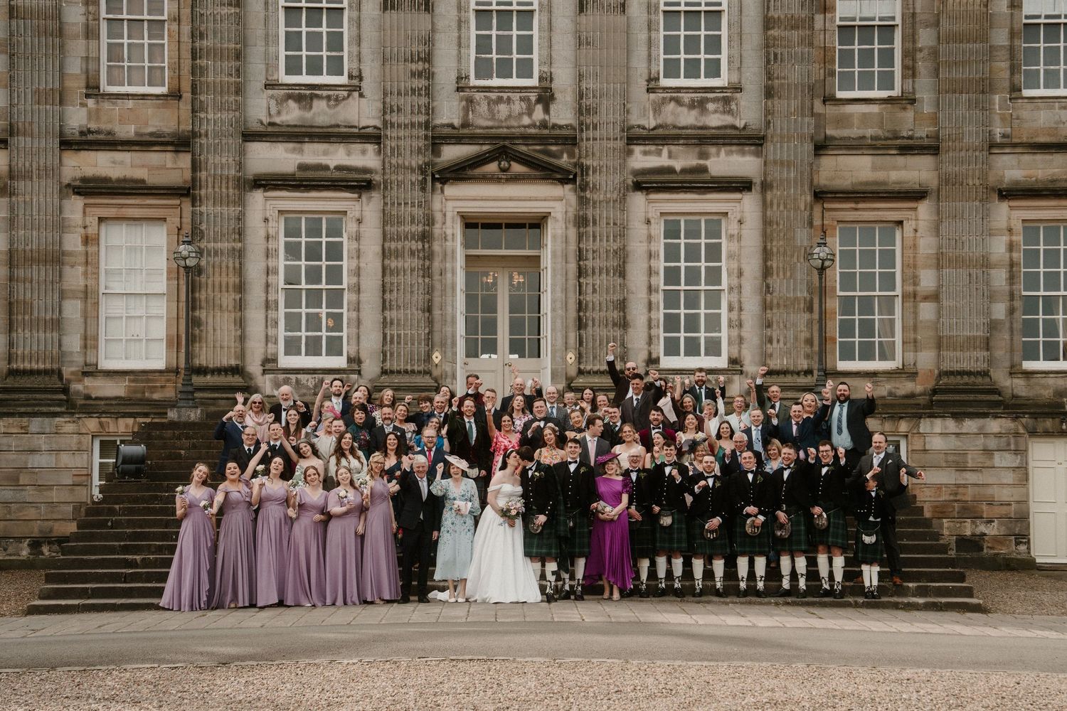 Wedding party poses on grand stone steps of historic mansion with classic architecture.