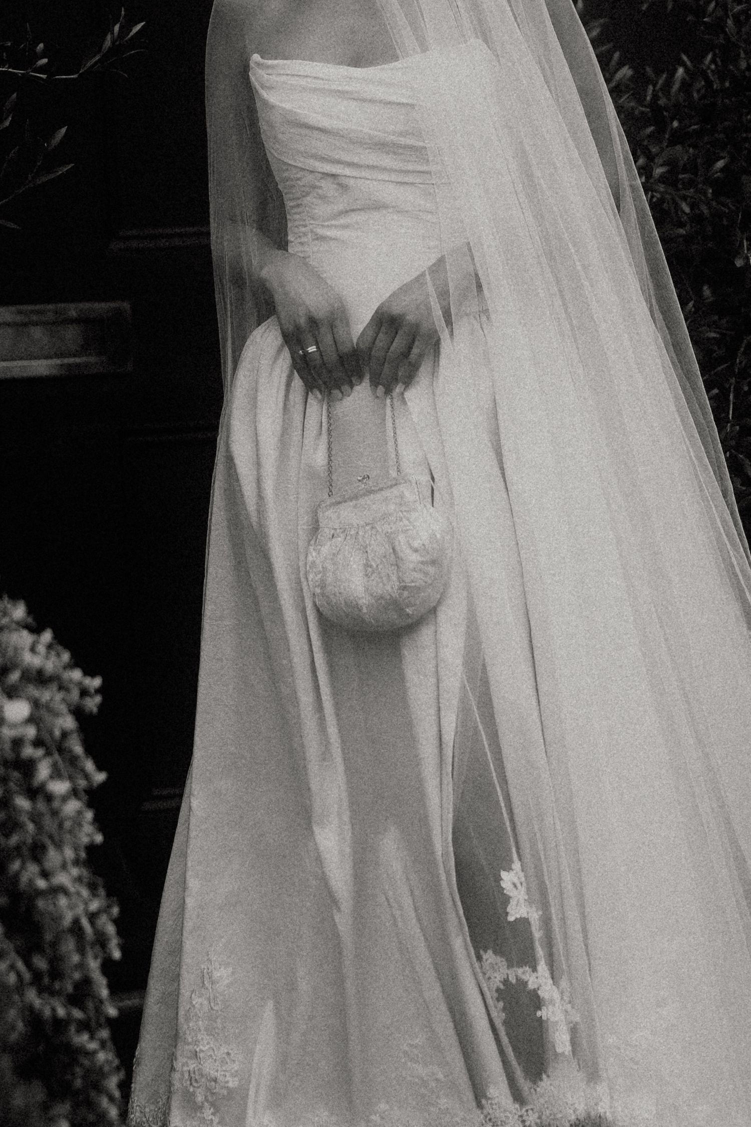 Close-up details of a white wedding dress with flowing tulle veil and delicate lace embellishments in a garden setting.
