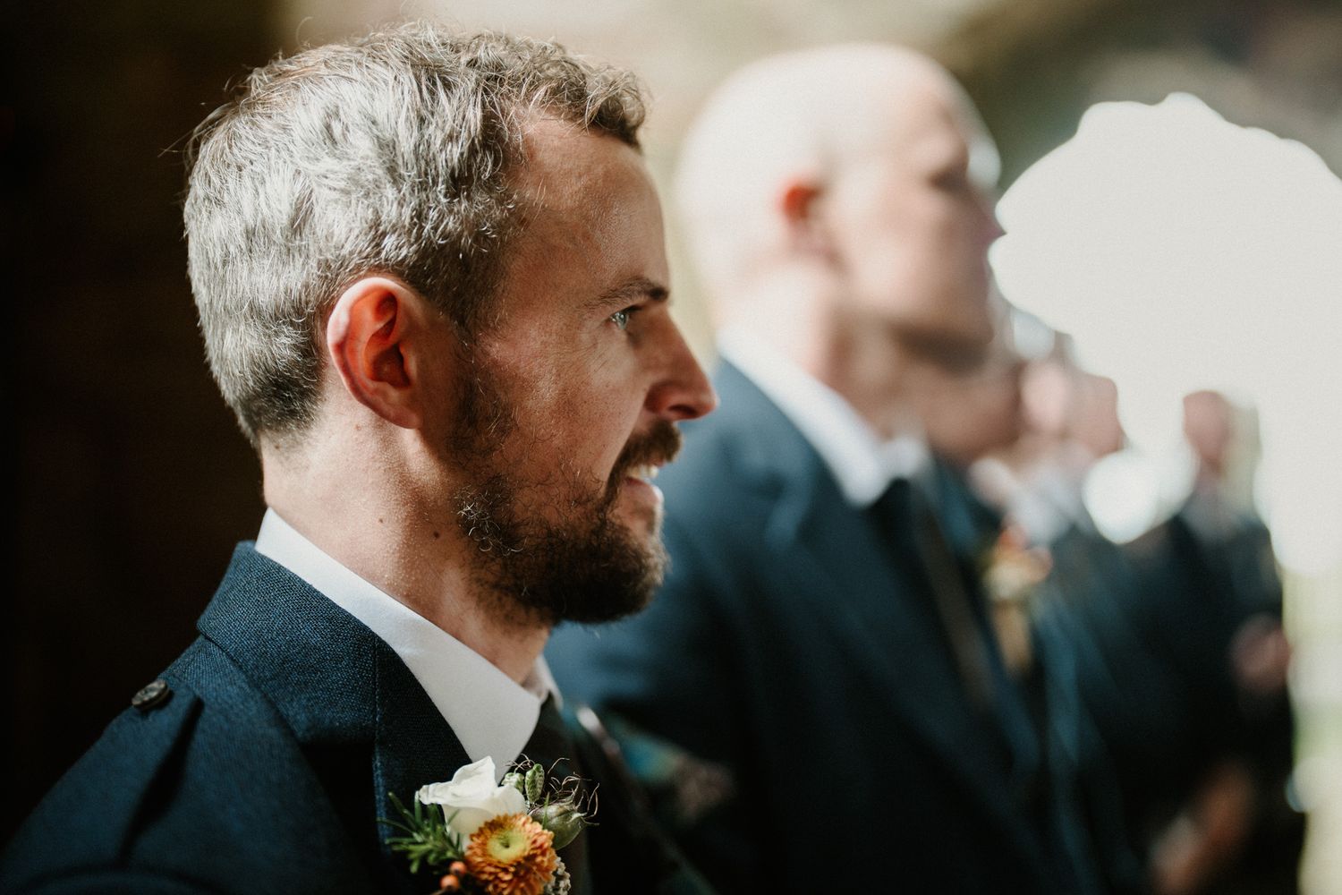 Close-up detail of wedding attire and boutonniere against blurred background.
