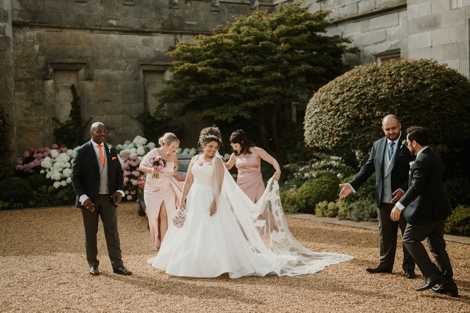 Candid wedding party moment captured outside gothic stone castle architecture.