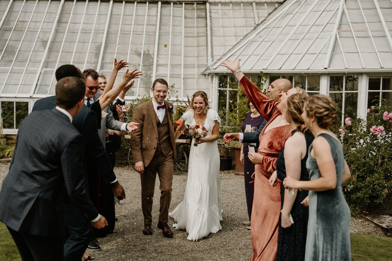 Joyful celebration outside vintage greenhouse with wedding party.