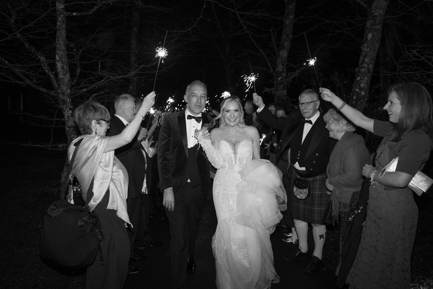 Guests celebrate with sparklers creating a magical nighttime scene at wedding reception.