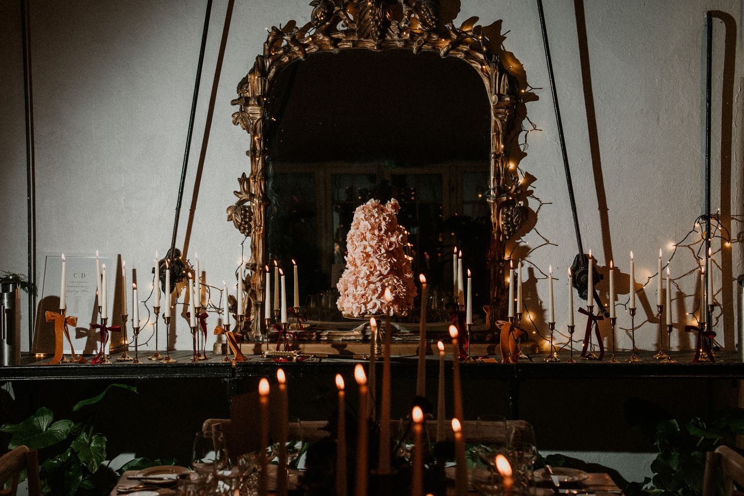 Elegant wedding reception table decorated with ornate gold mirrors, floral arrangements and glowing candlelight.