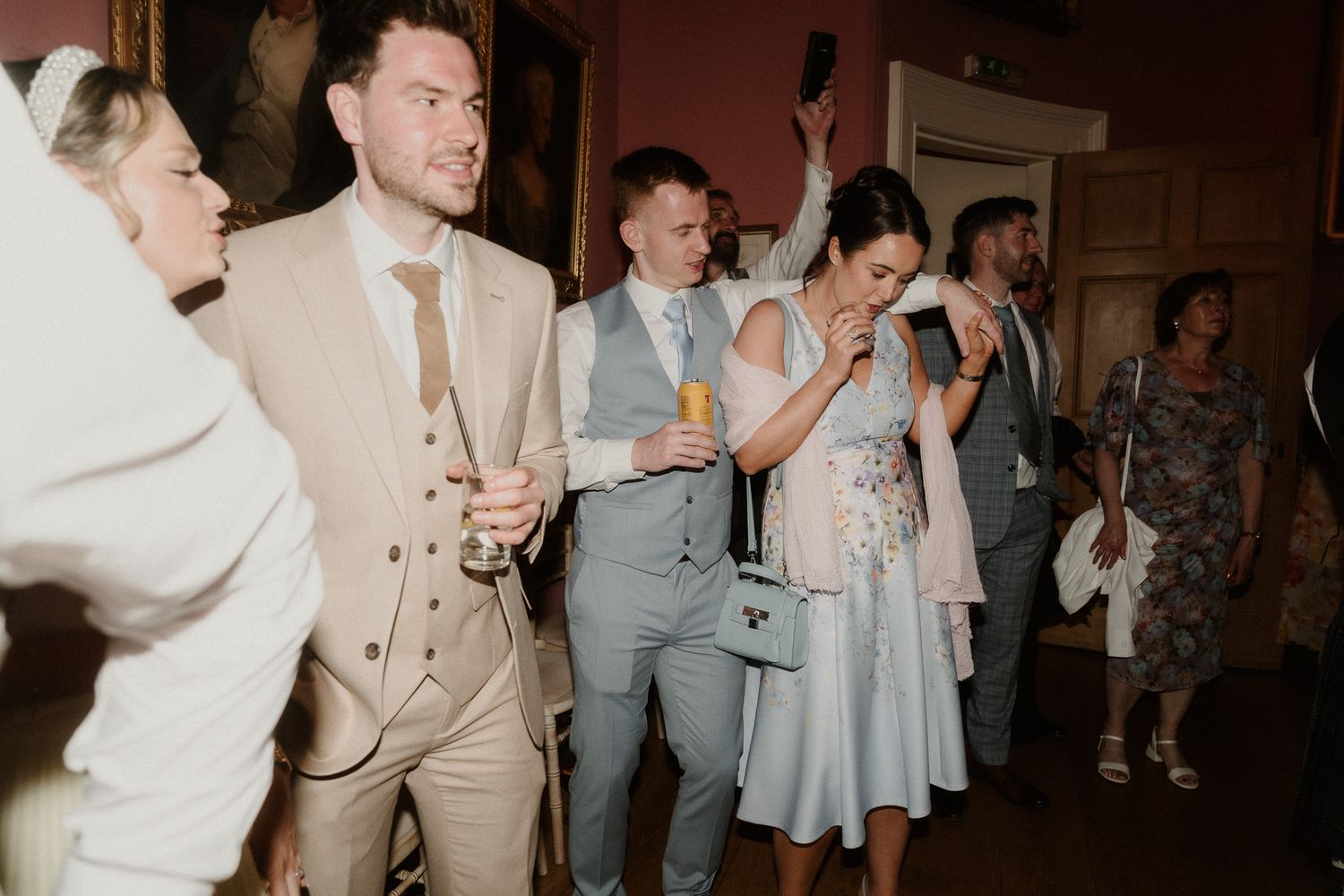 Wedding guests celebrate and dance in ornate venue, dressed in elegant formal attire.