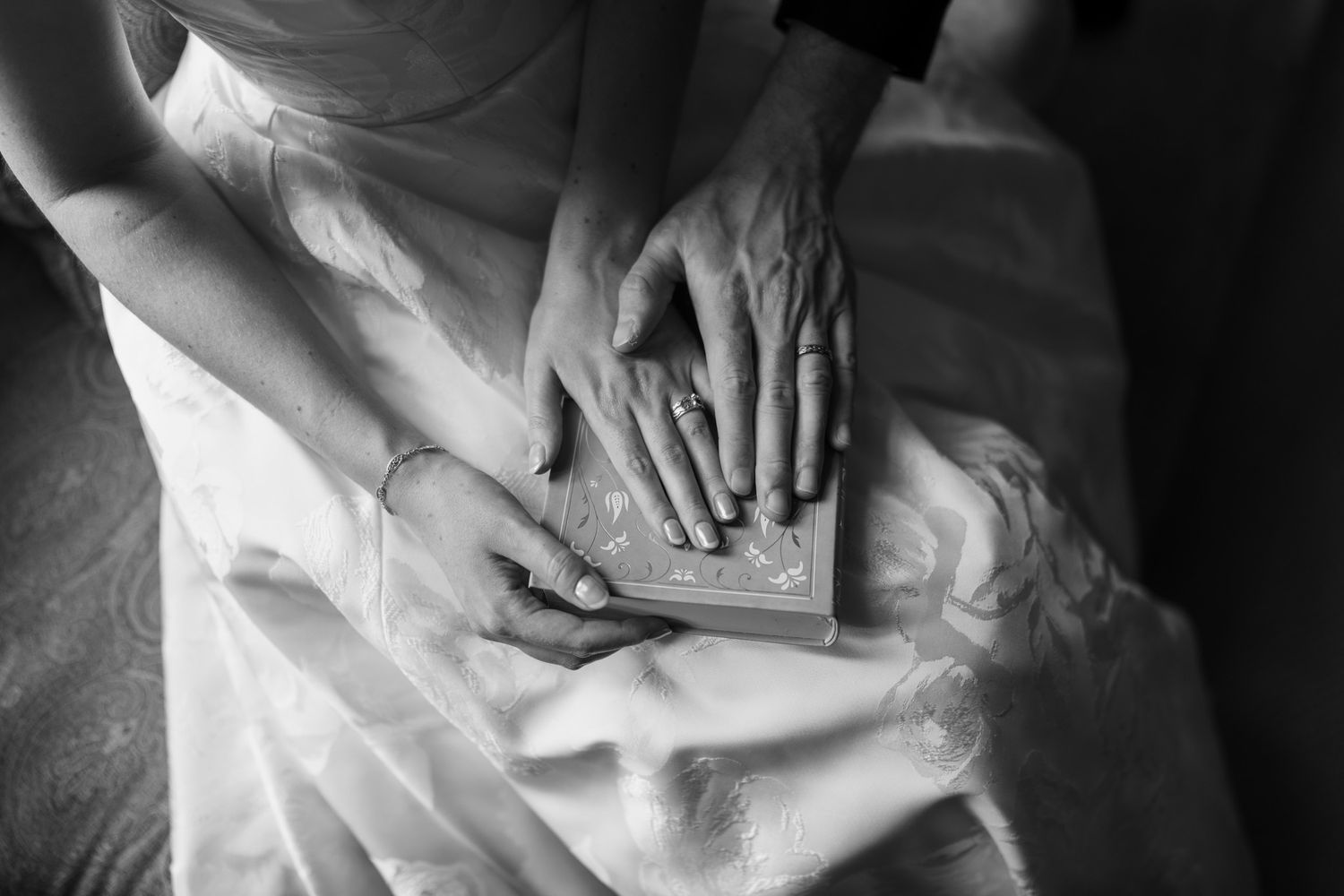 Black and white photo of bride and groom hands with wedding rings resting on a decorative book.