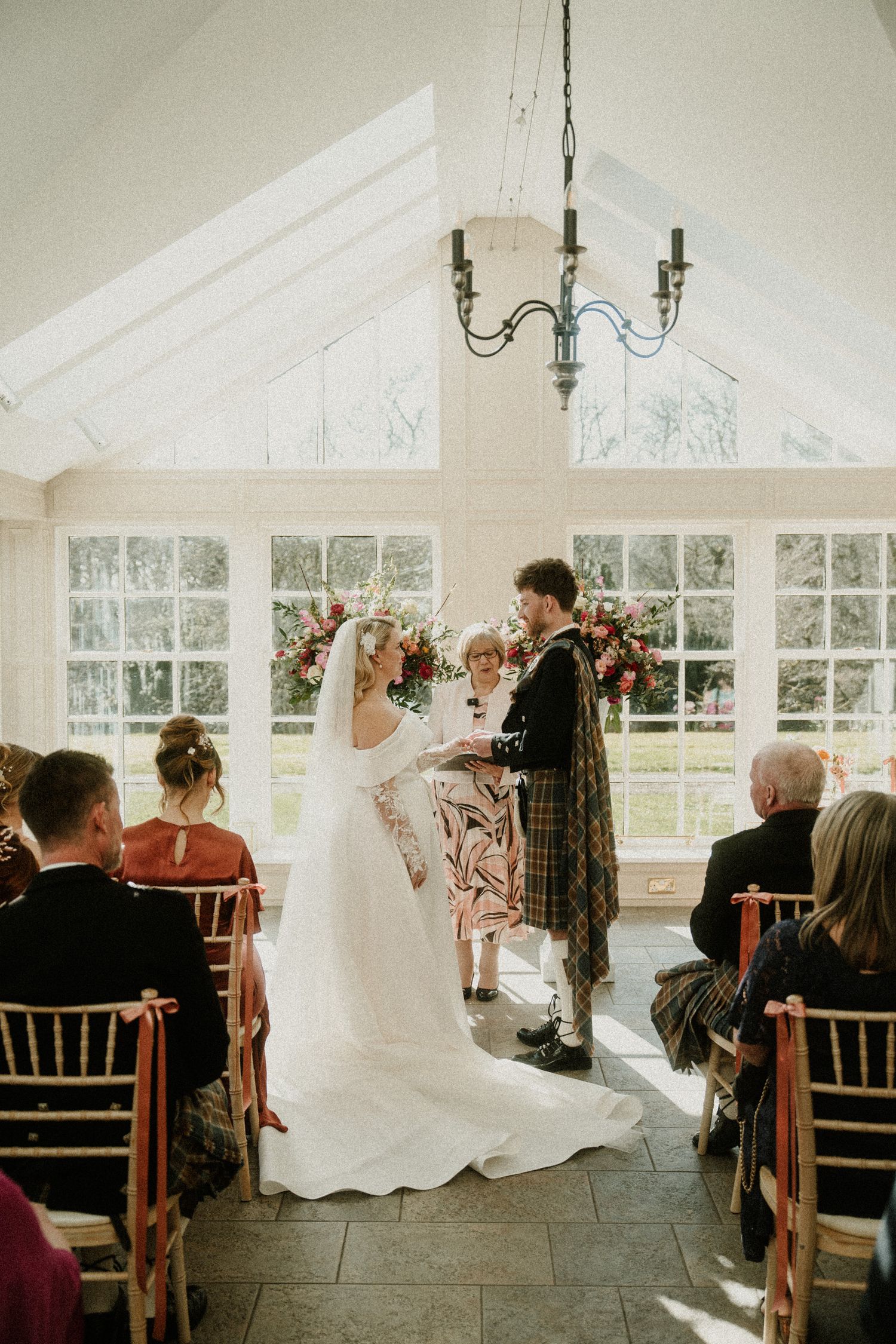 Wedding ceremony in bright white venue with vaulted ceiling and large windows.