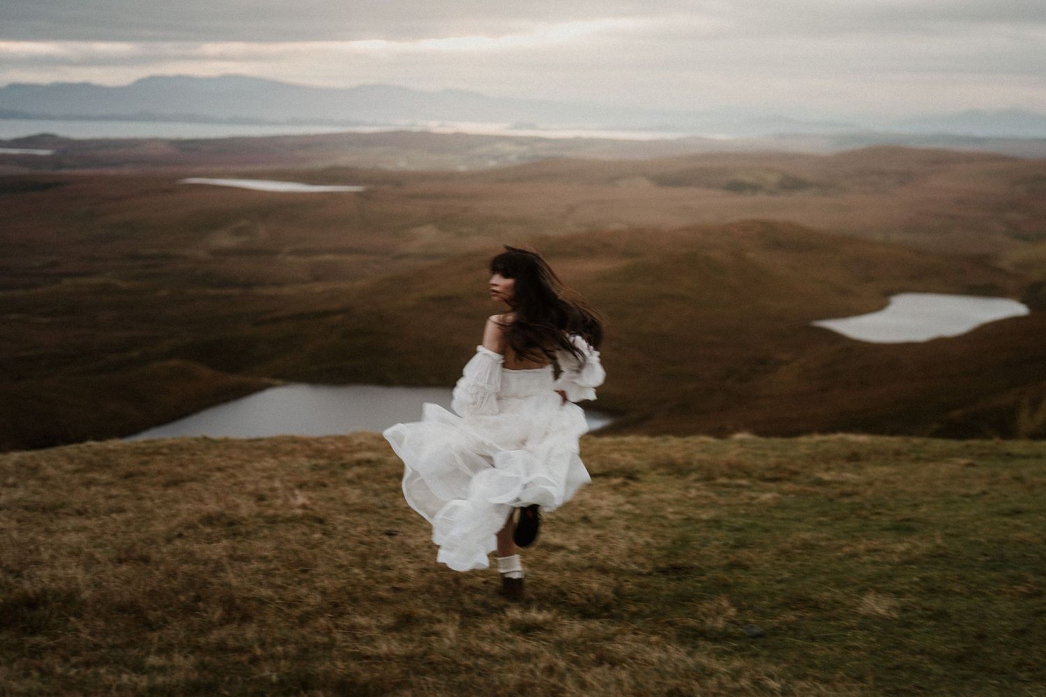 Sweeping landscape view of highland moors with dramatic cliffs and remote lakes in distance.