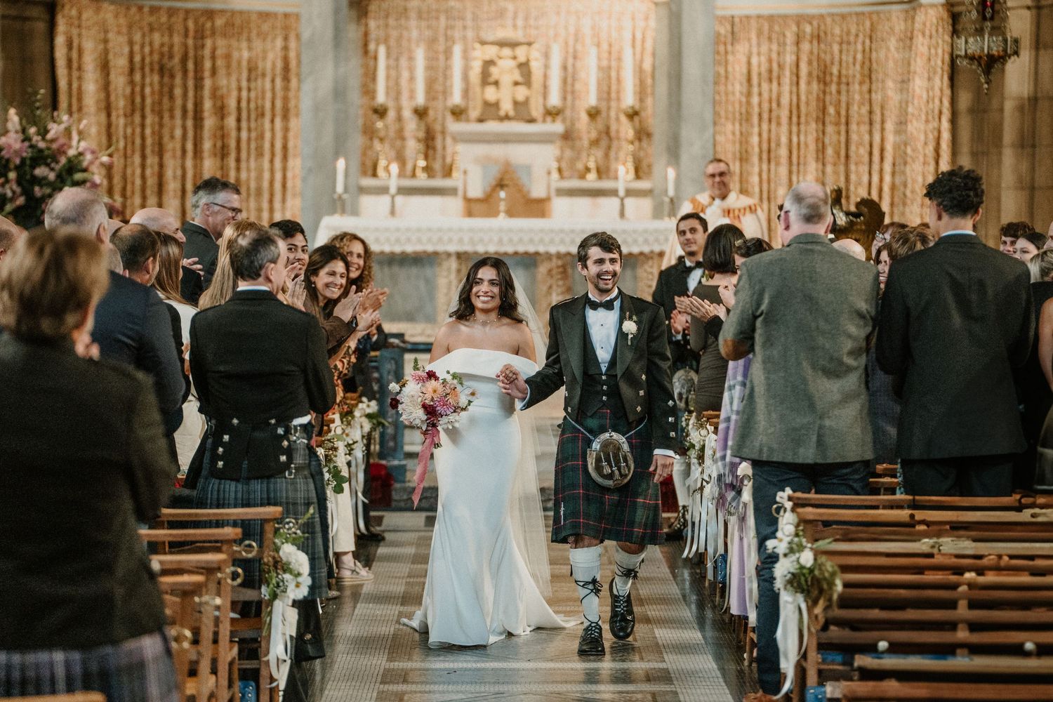 Wedding ceremony taking place in an elegant church with gold curtains and wooden pews.