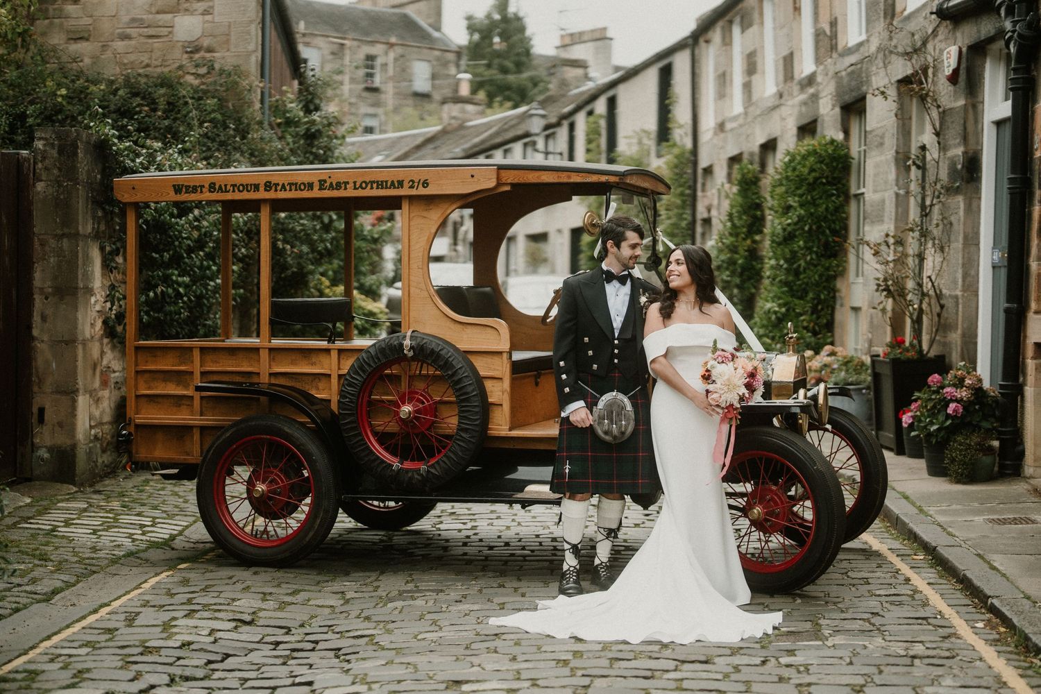 Classic wooden car and motorcycle frame elegant bridal portrait on cobblestone street.