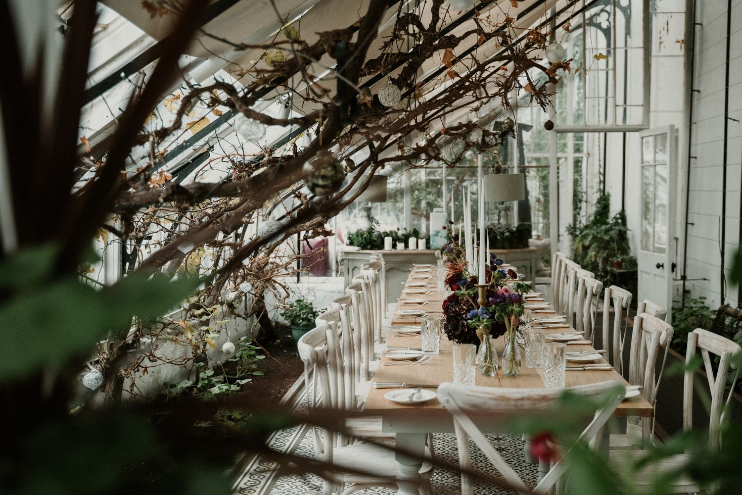 Wedding reception setup in a greenhouse with natural light streaming through glass panels.