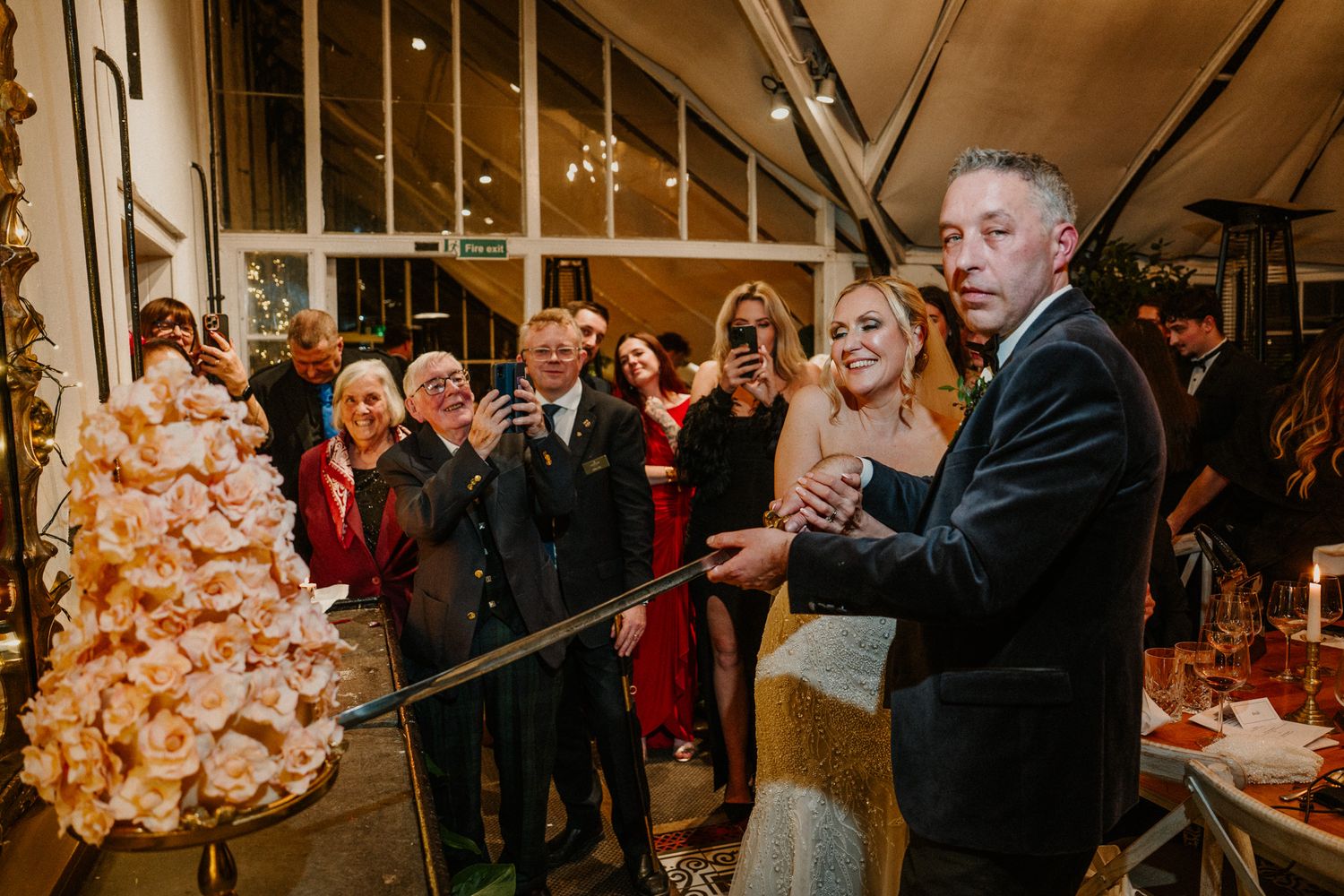 Wedding reception guests gather around tables with phones capturing special moments.