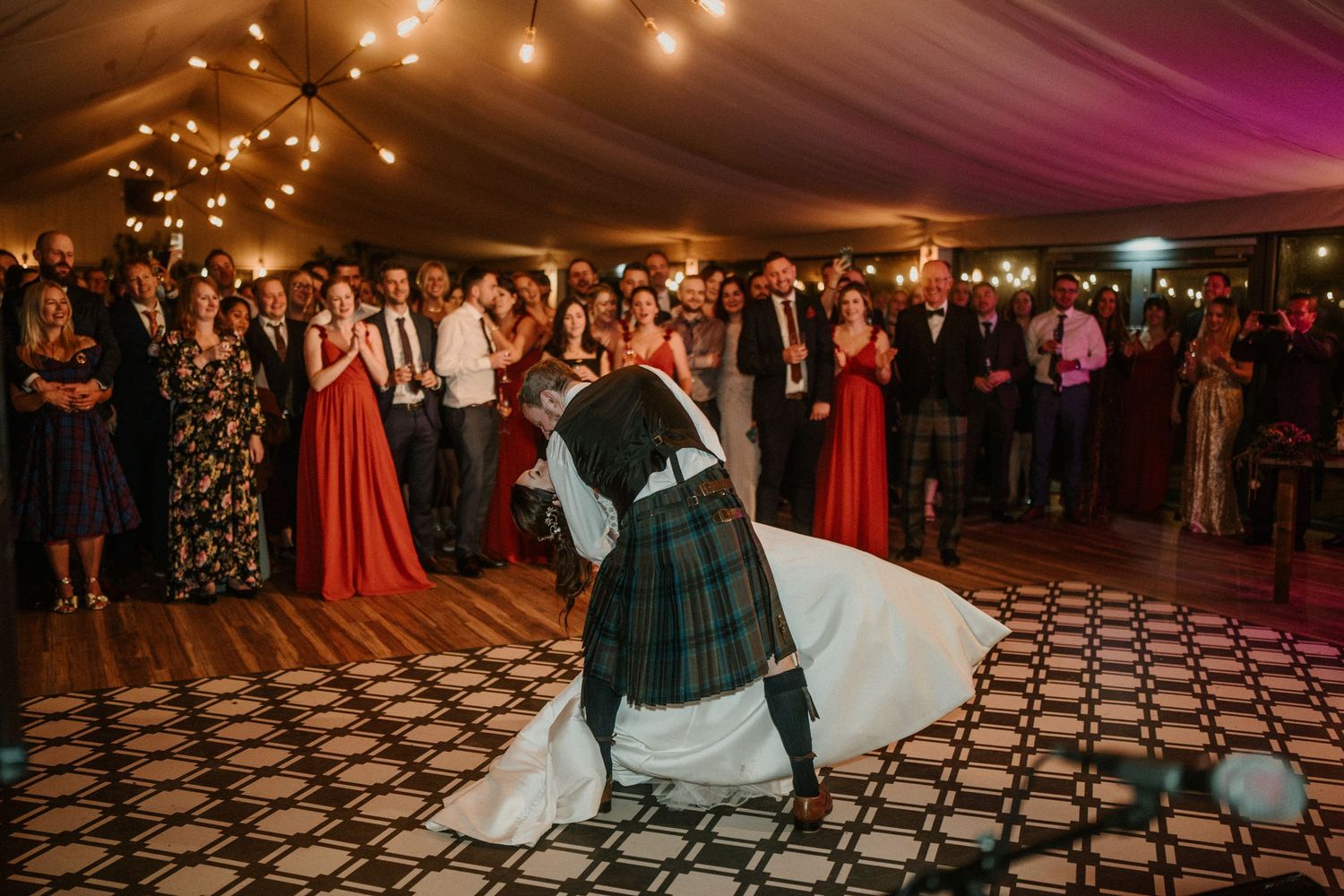 A Scottish wedding celebration with guests watching the couple dance on a patterned floor.