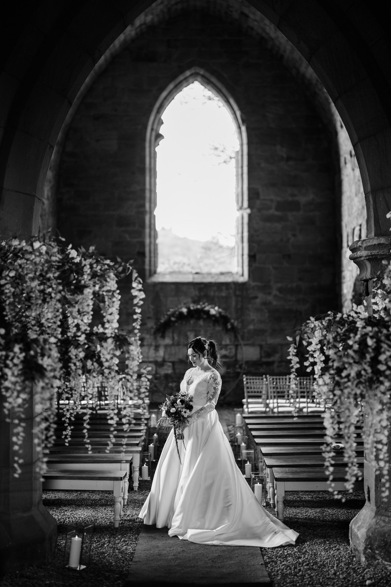 Black and white wedding portrait in gothic church interior with arched windows and floral decor.