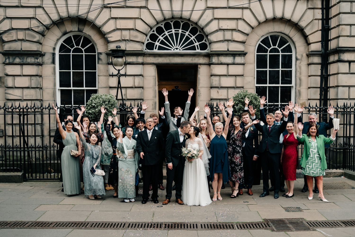 Wedding guests gathered outside historic building with ornate architecture and columns.