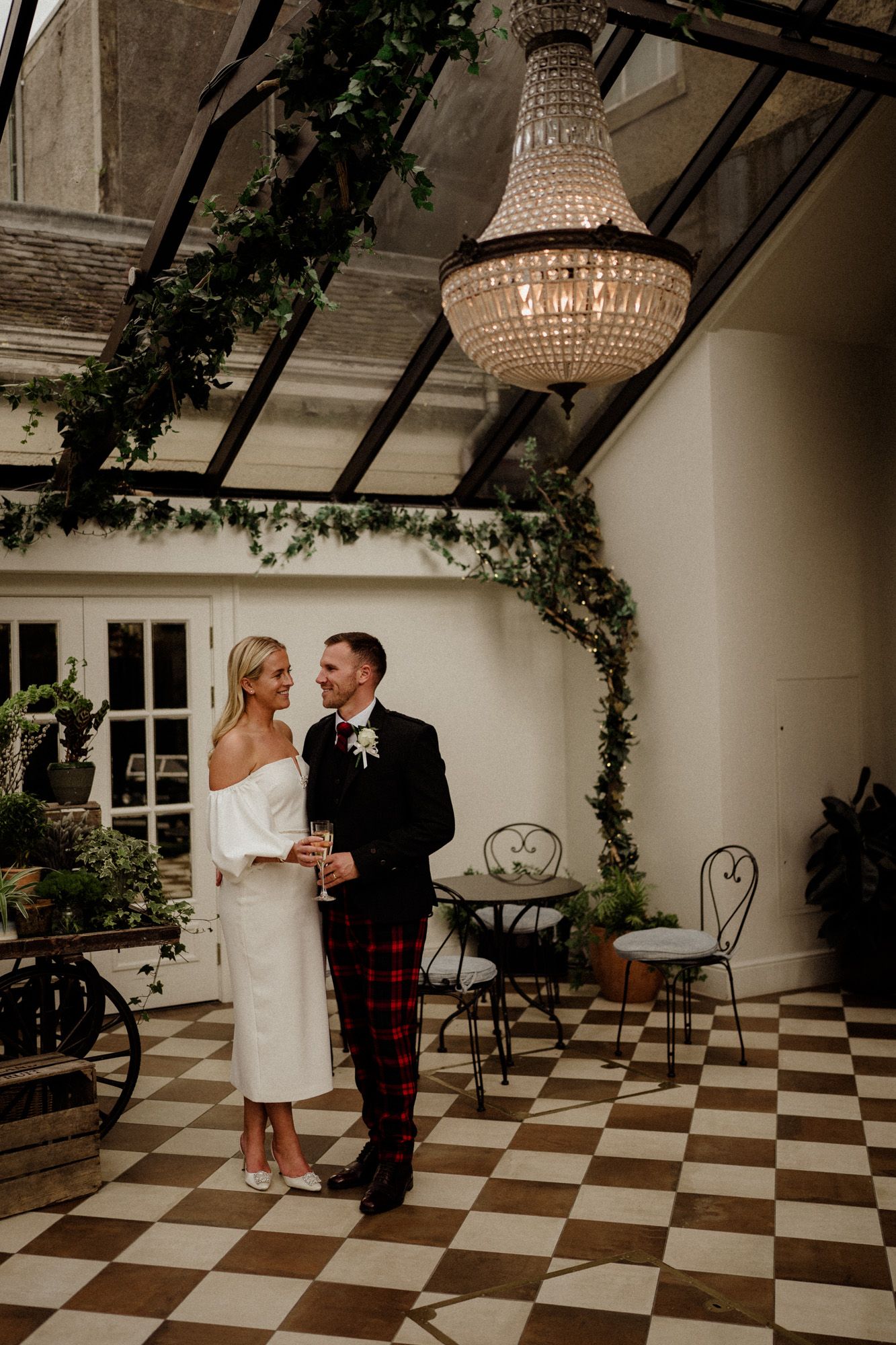 Romantic dance scene on a checkered floor with greenery and chandeliers overhead.