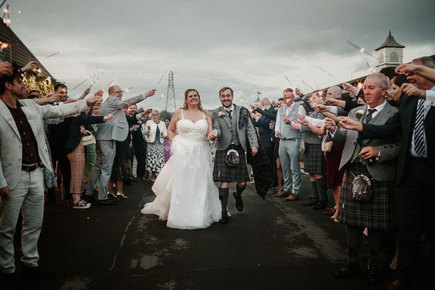 Wedding celebration exit with guests throwing confetti under dramatic sky.