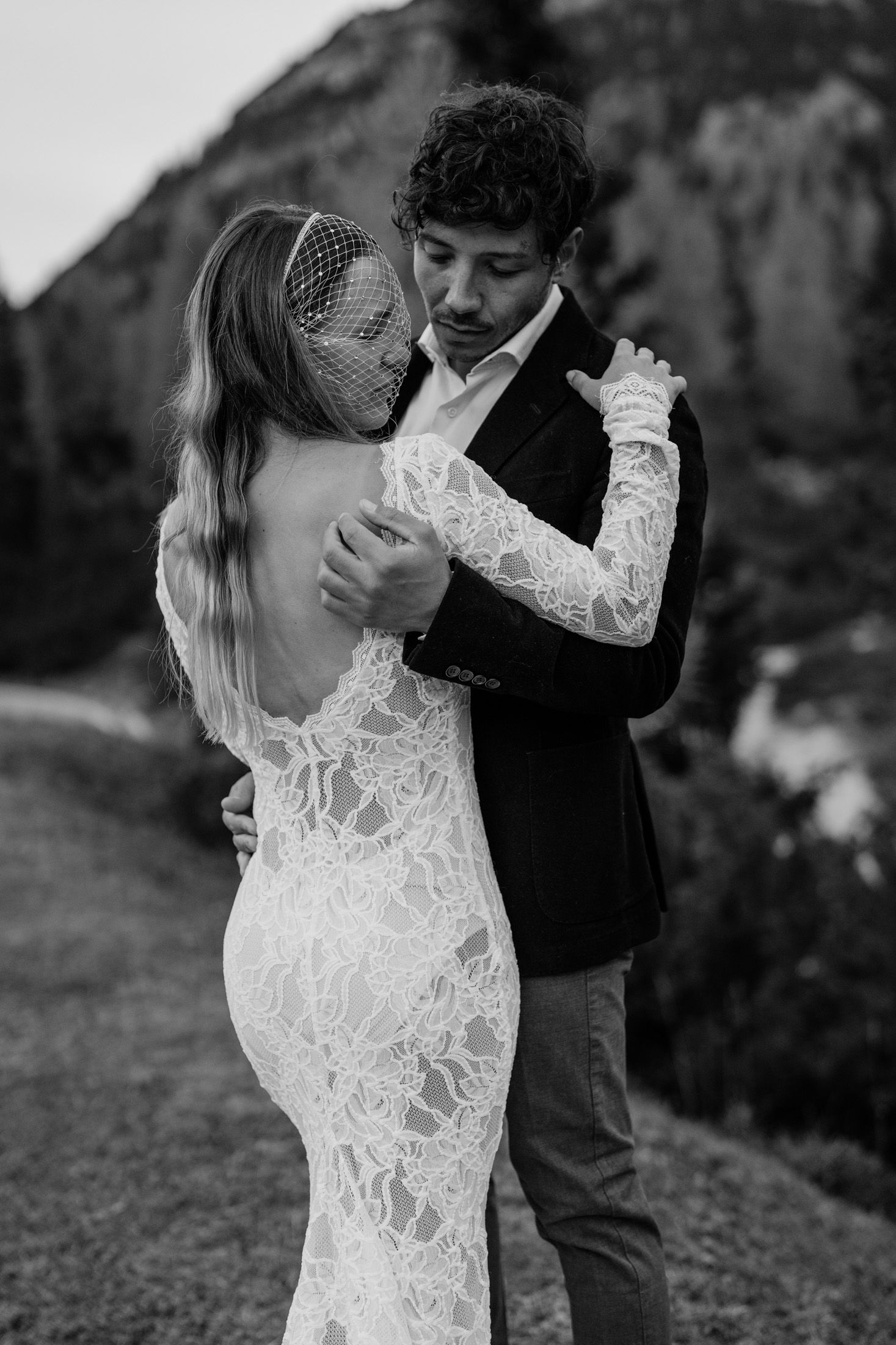 A couple in wedding attire dances intimately with rugged mountain peaks in the background.