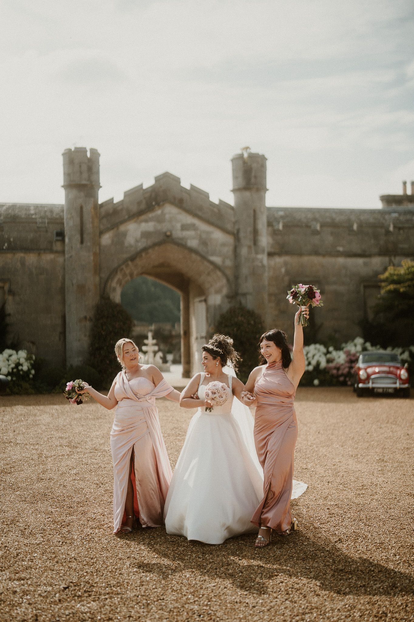 Wedding party in pink bridesmaid dresses and white gown pose playfully on castle grounds.
