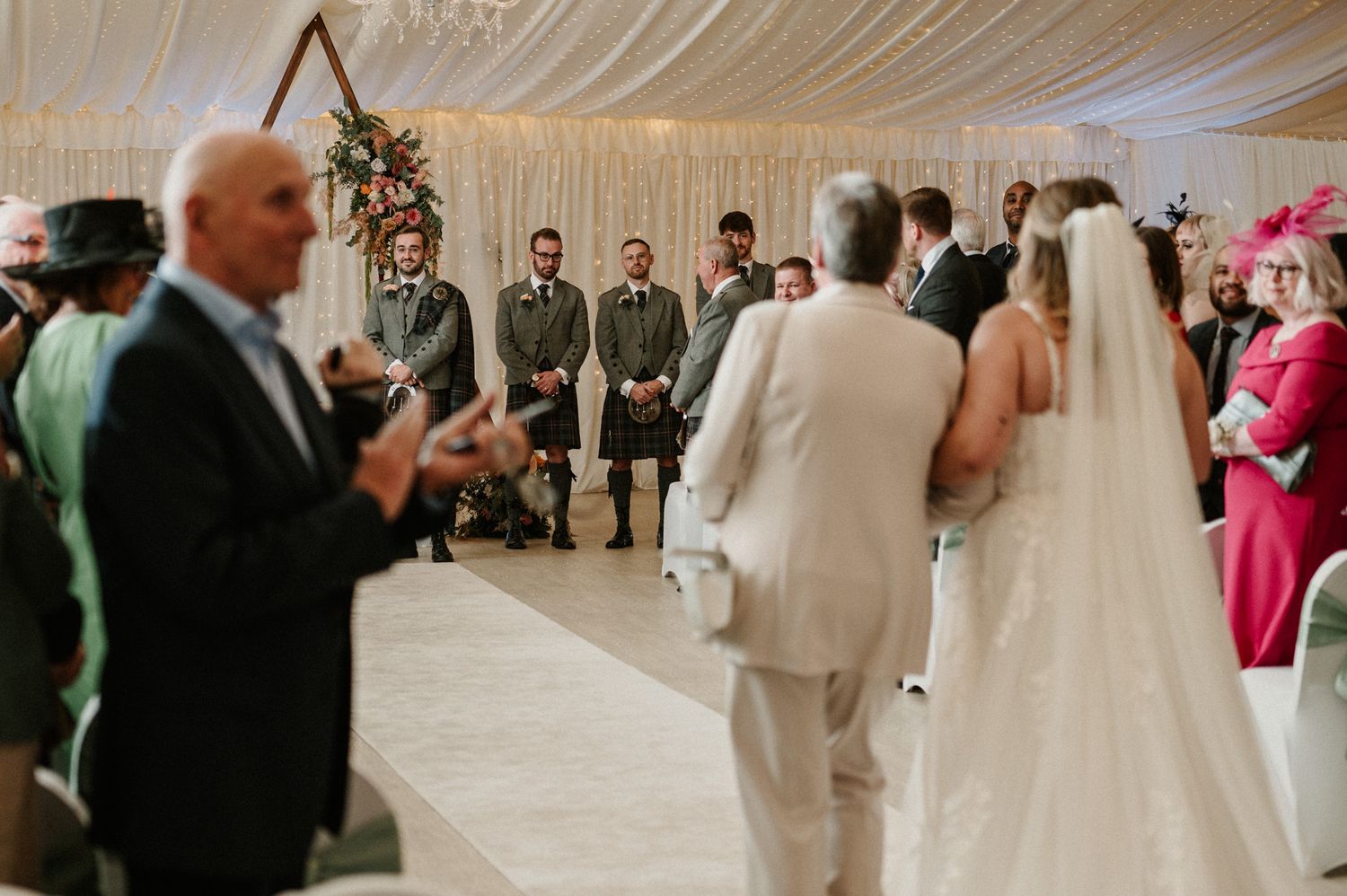 Wedding ceremony setup in an elegant white draped room with rows of chairs and floral arrangements.