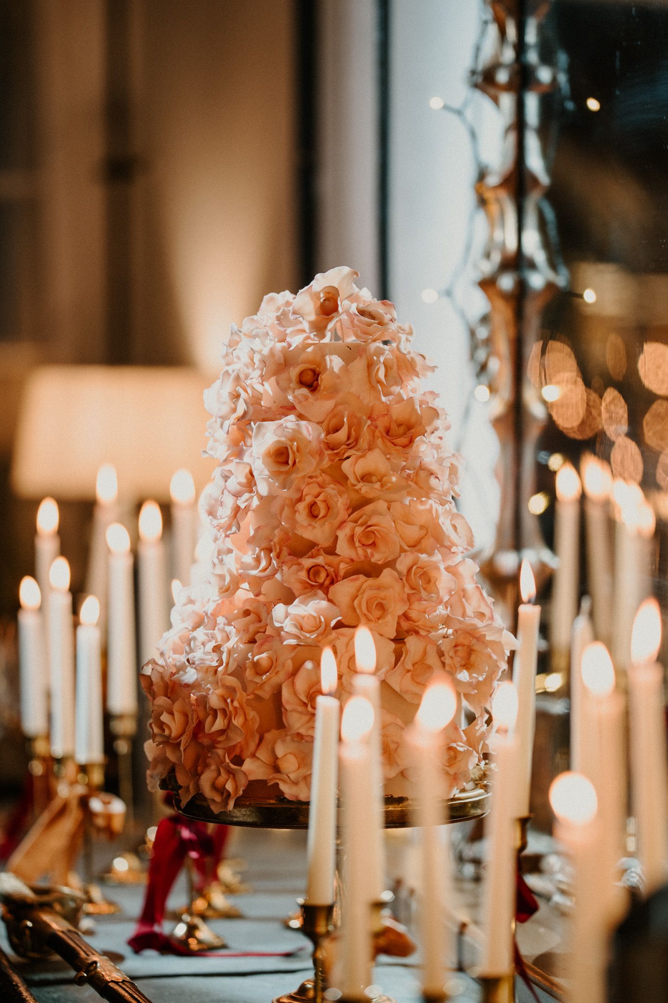 White taper candles line a formal dining table with lush peach floral arrangements.