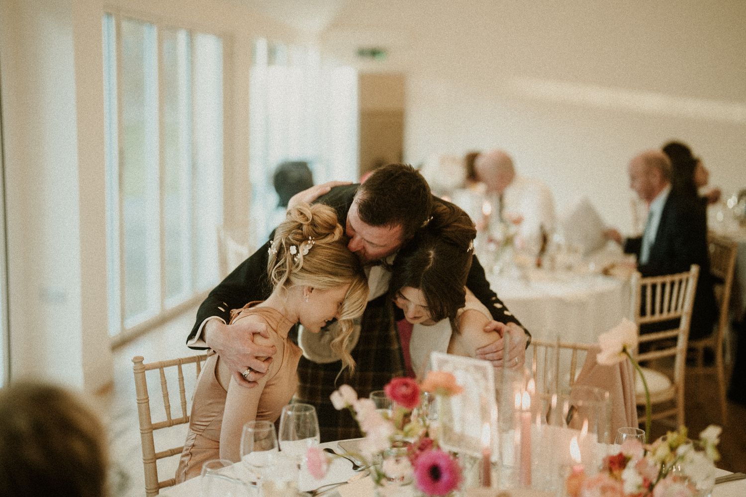 Guests seated at decorated wedding reception tables with pink floral centerpieces.