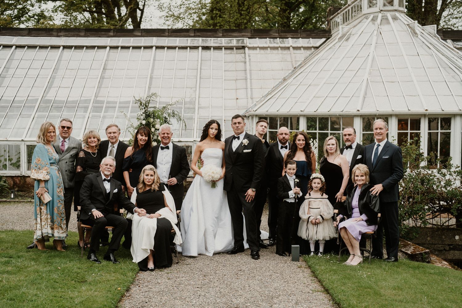 Wedding party poses together in front of a beautiful greenhouse conservatory with white floral decorations.