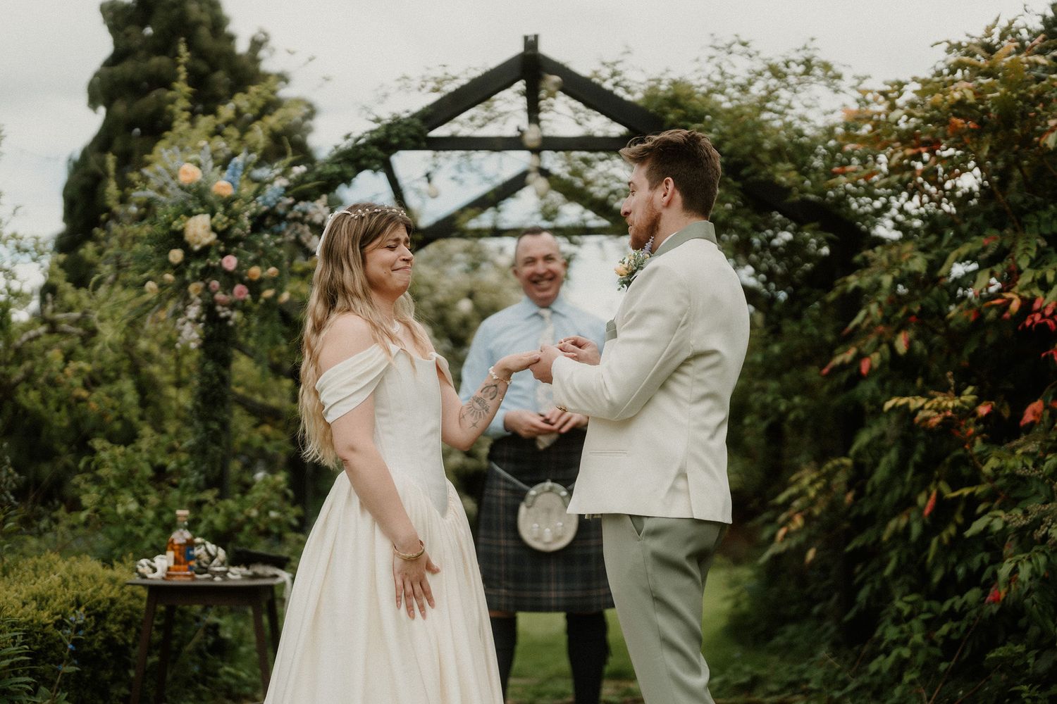 Couple exchanging vows outdoors in a lush garden wedding ceremony with a officiant in a kilt.