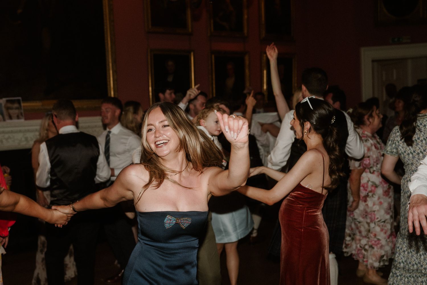 Guests dancing joyfully at a wedding reception in an elegant venue, woman in blue dress laughing with arms raised.