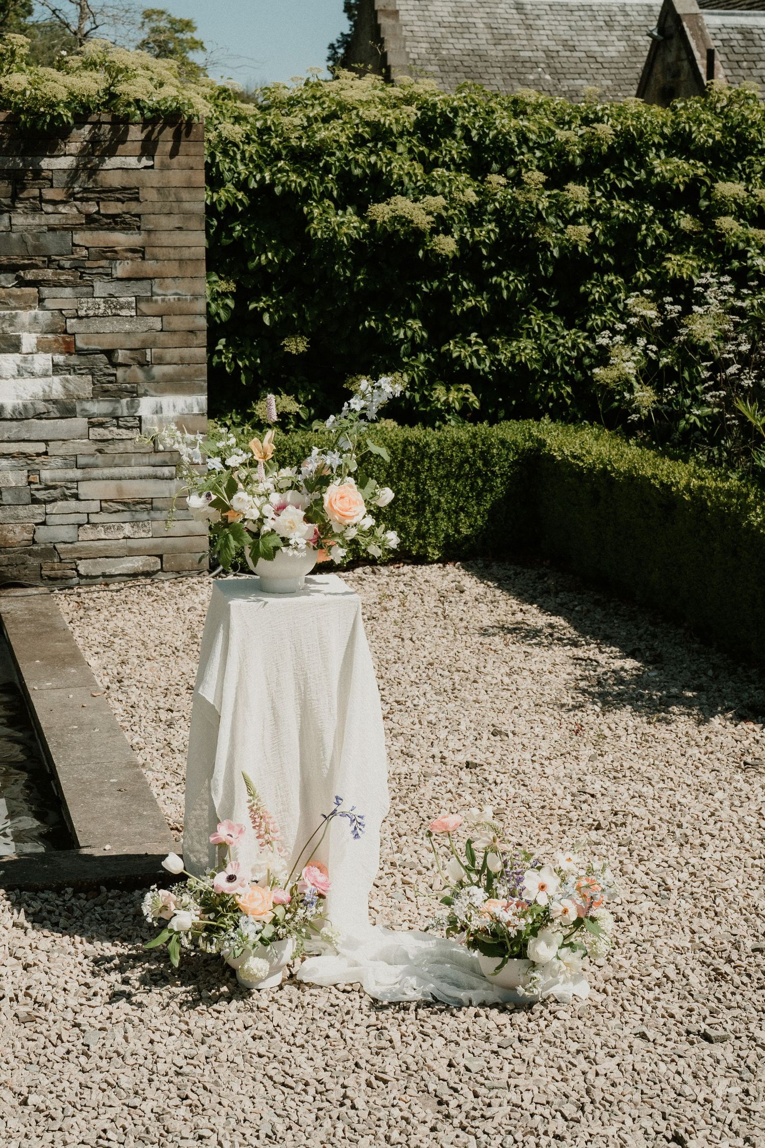 Outdoor wedding reception setup with white linens and floral arrangements on gravel patio.