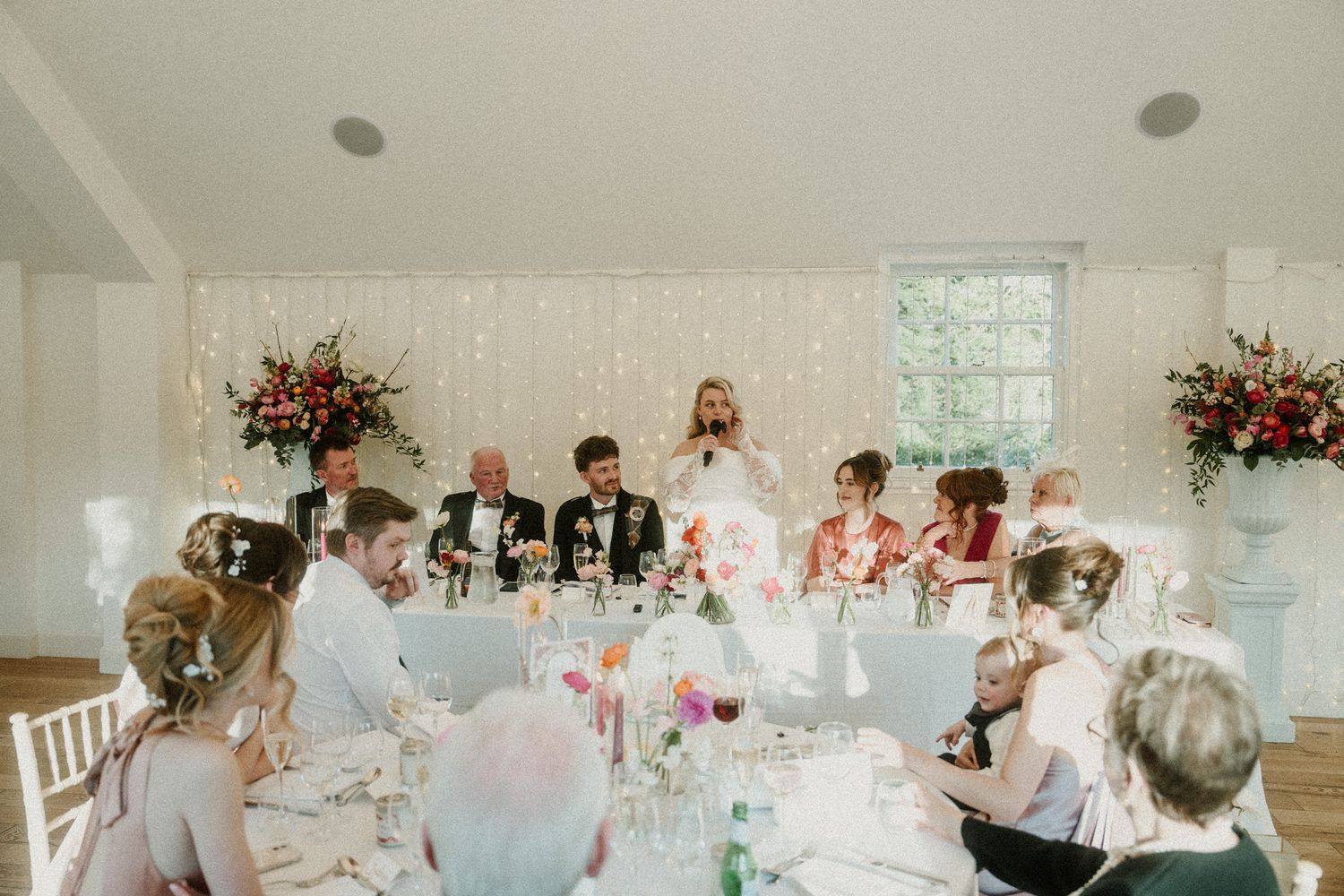 Wedding reception tables set with elegant decor and floral arrangements in a bright venue.