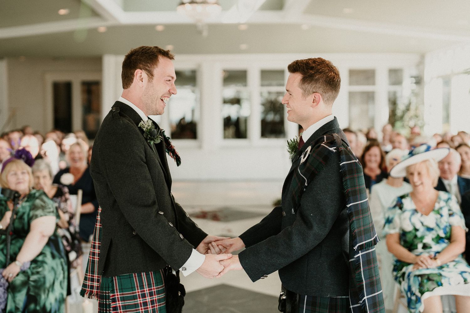 Wedding celebration scene with guests in formal attire and kilts in a bright venue.