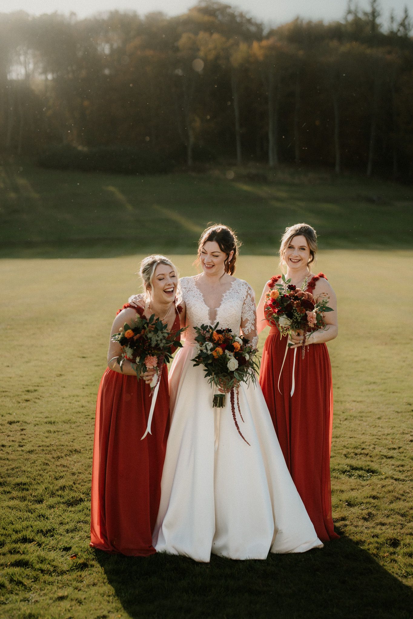 Joyful wedding photo of bride in white gown with bridesmaids in red dresses at sunset.