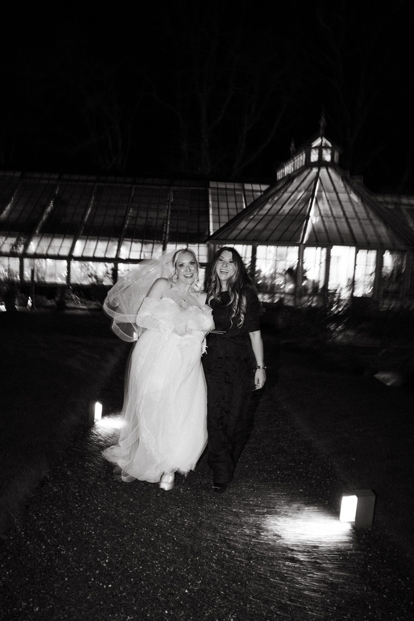 Nighttime wedding scene with illuminated greenhouse structure in background.