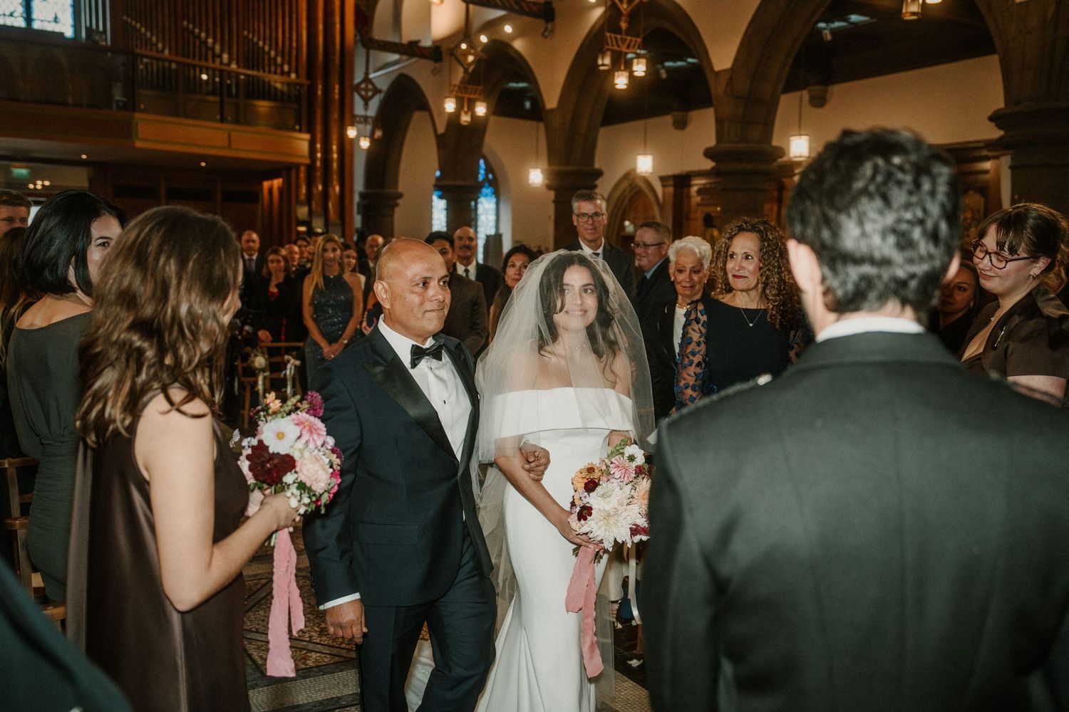 Wedding ceremony in progress inside historic church with arched ceilings and elegant lighting.
