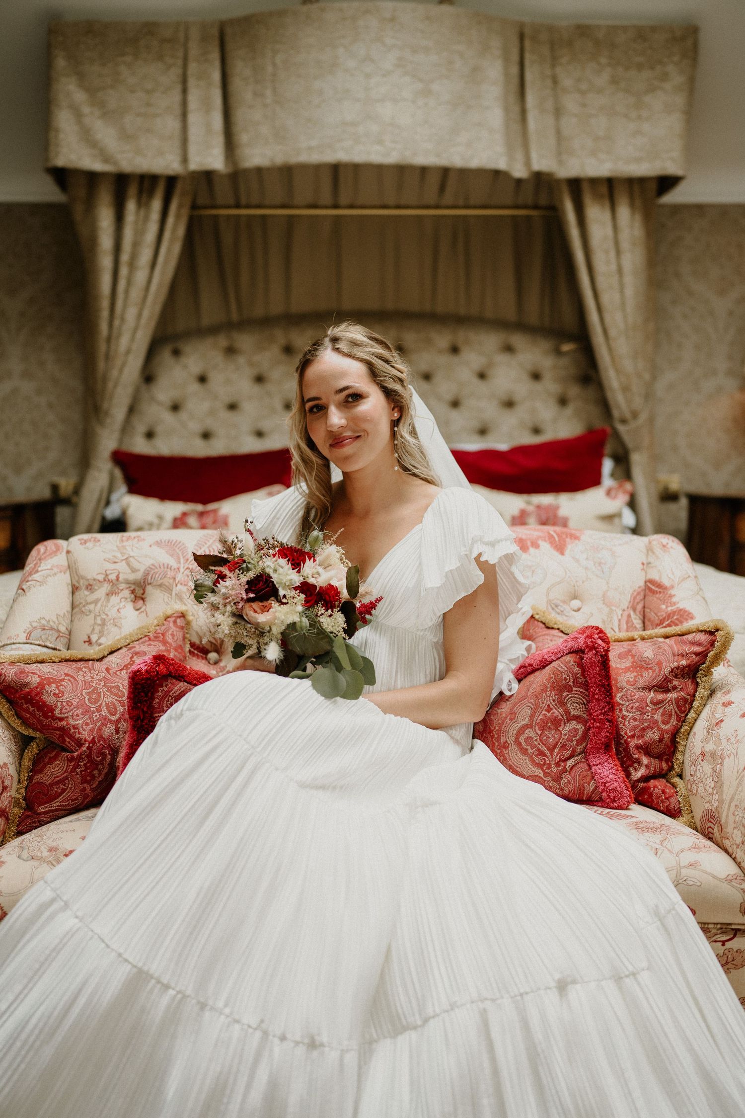 White wedding dress spread across luxurious red and cream sofa.