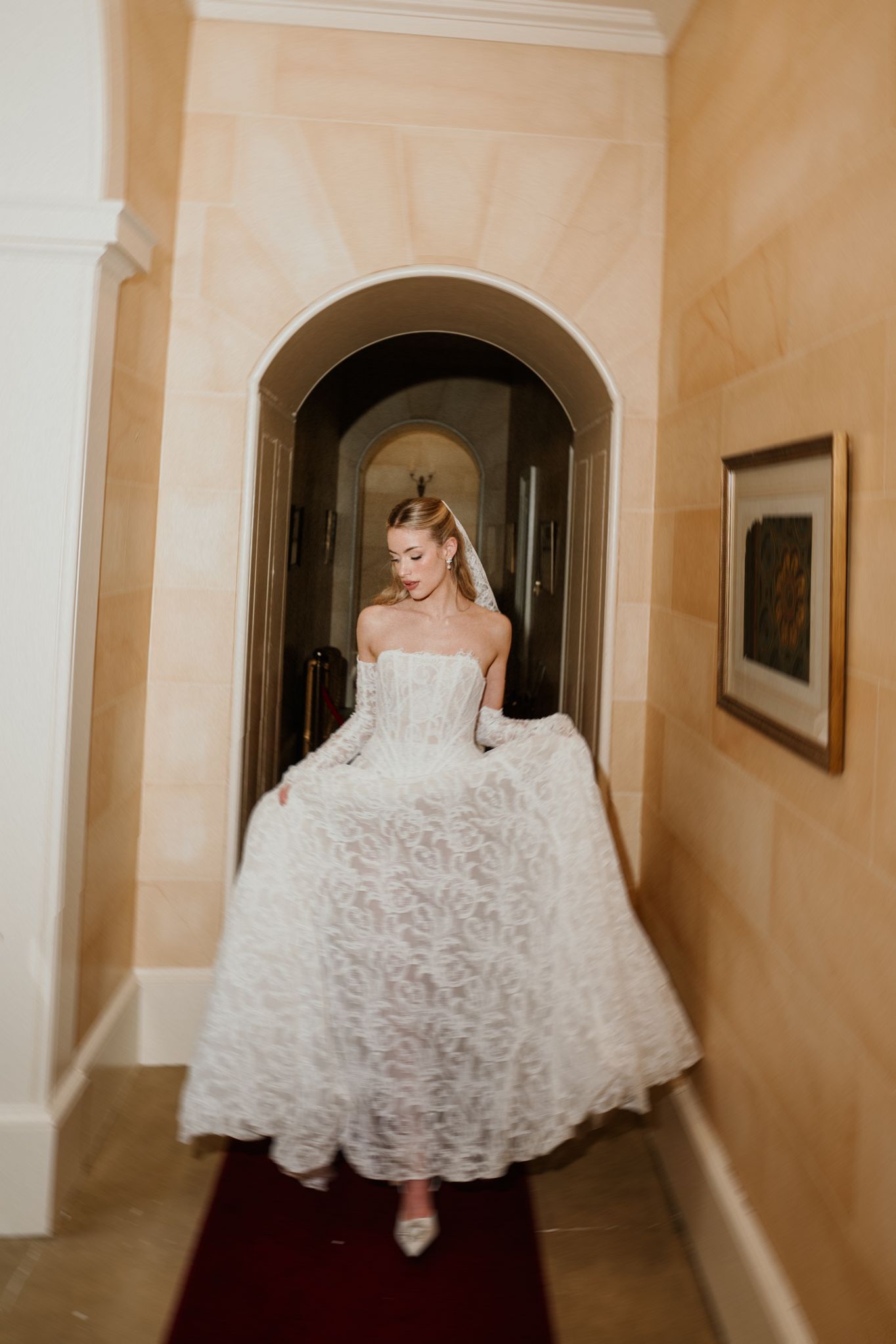 A bride in a white lace wedding dress twirls playfully in an elegant hallway showing the full skirt of her gown.