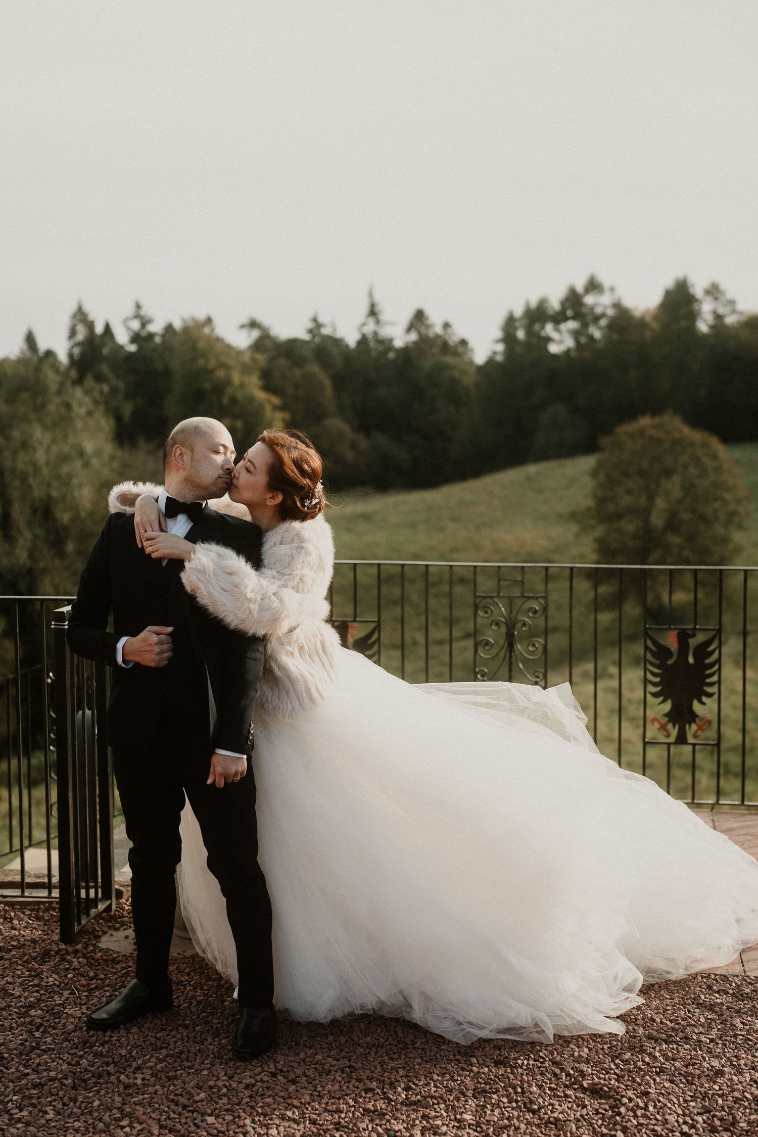 A couple in formal attire dances together on a stone patio surrounded by trees.