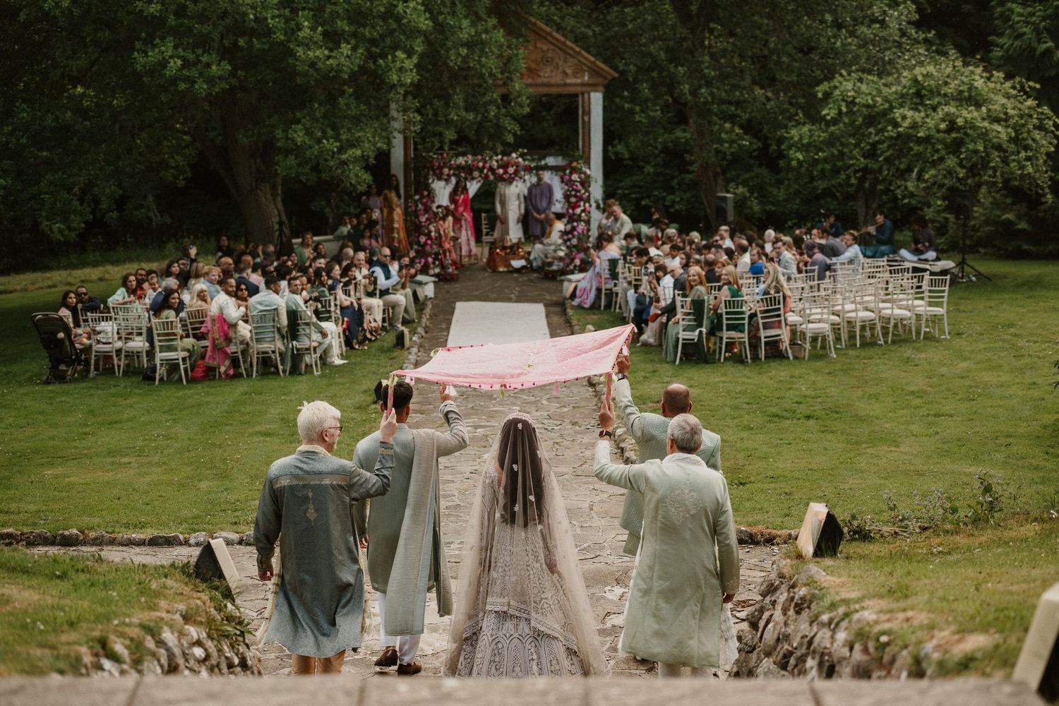 Wedding ceremony setup with rows of white chairs along garden pathway leading to altar.