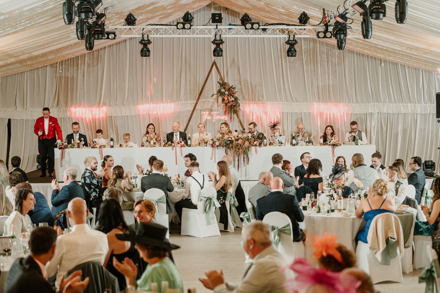 An elegant wedding reception under a white tent with guests seated at decorated tables.