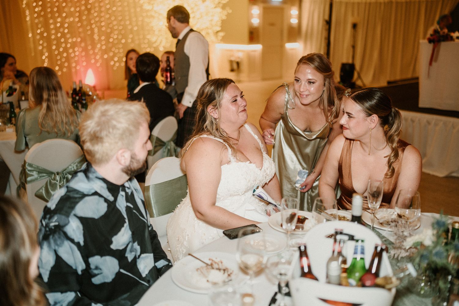 Wedding reception table conversation with warm fairy light backdrop.